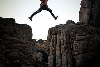 a girl is trying to jump from one rock to another