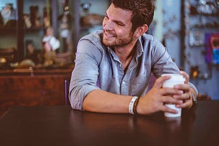 Man smiling, holding white cup.