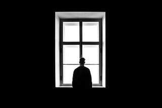 black and white picture of a man lost in thoughts in front of a window