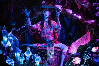 Fantastic image of a shaman, arms outstretched looking up. “Avatar” like figure surrounded by indigo coloured crystals and violet shapes, dark background.