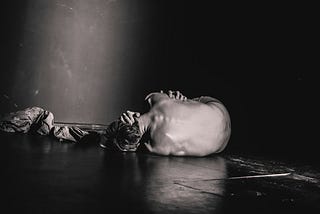 a grayscale image of a man laying on the floor, holding himself in pain.