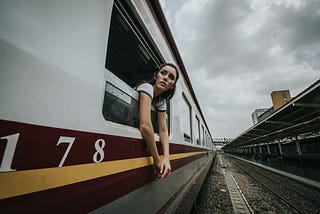 A woman hangs out of a passenger train, looking concerned.