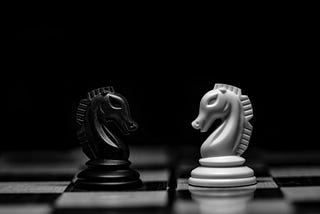 A black and white photo of two chess knights on a chessboard facing each other.