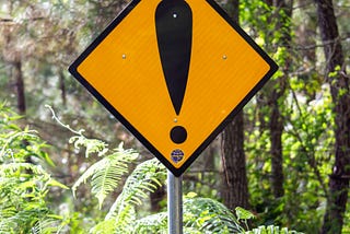 Yellow warning sign on a post with no words on it, only a large black exclamation mark.