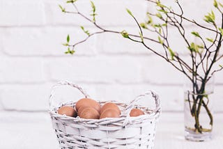 a basket of eggs beside a vase of sprouting branches