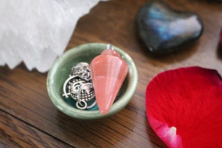 this is a photo of some crystals including a pink pendulum in a bowl.