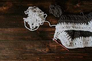 A crochet needle is looped into a gray and white project. White and gray bundles of yarn sit attached to the project.