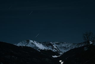 Snowy mountains at night with stars shooting across the sky.