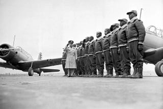Mickey Markoff Air Sea Exec 2024 — black and white photo of Tuskegee Airmen in uniform in front of military aircraft. Men wearing bomber jackets and hats with other person wearing trench coat and hat. Posted on 2024 Mickey Markoff article on black history month in aviation