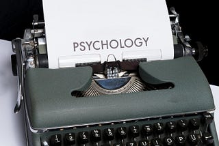 An antique typewriting with a sheet of paper that says, “Psychology”, sits on a table.
