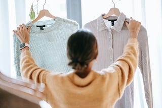 Woman holding up a formal shirt and an informal sweater, confused which to wear.