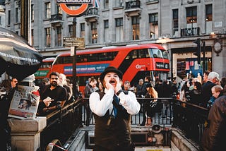 A dapper fella standing in the middle of London yelling.