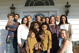A group picture of a multi-generational family, standing in front of a white building.