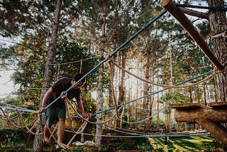 A man navigating a ropes course in a forest.