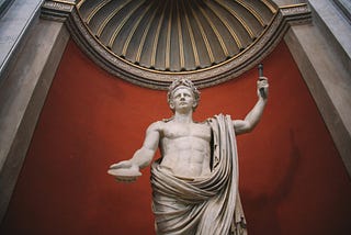 A laurel-wreathed marble statue stands in a Roman temple, holding a stick aloft in one hand, and a shell in the other