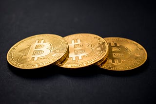 Three physical coins with the Bitcoin logo on them.
