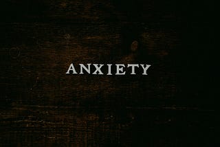 The word “Anxiety” is written across some dark-stained wood.