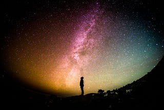 silouette of a person looking up at an awesome expance of the sky at night. Milky way is central.