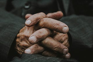 A pair of elderly male hands, fingers intertwined