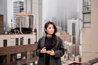 Professionally dressed woman on a New York rooftop with a foggy skyscraper-filled cityscape behind her