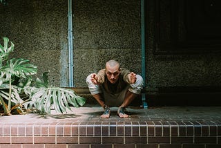 Man squatting in an advanced yoga pose, confronting the camera