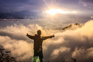 Man facing clouds during golden hours. He is on the top of a mountain.