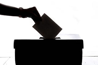 A silhouette of a hand placing a piece of paper in a ballot box.