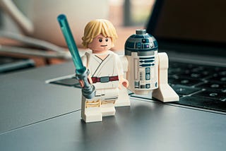 Luke Skywalker with a blue sabre and R2D2 Lego standing on a laptop.