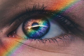 A photograph of an eye with the reflection of a rainbow on it.