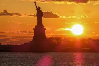 The Statue of Liberty against an orange sunset.
