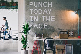 A picture of an office, and on the wall it says in bold letters, “PUNCH TODAY IN THE FACE.”