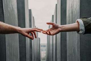 The hands of two people, separated by distance, but close enough that they can barely touch