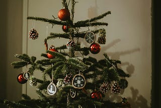 A spindly, sparse real Christmas tree with red bulb ornaments and gold snowflake ornaments.