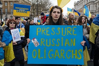 A woman at a protest holding a sign that says, “Pressure Russian Oligarchs”