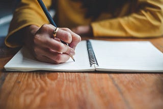 A person writing in a notebook with a pencil