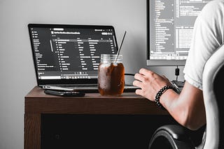 a software engineer sitting on his disk and work with 2 screens and a cold dark drink