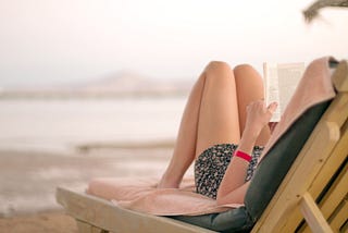 Woman lying on the beach, relaxing and reading