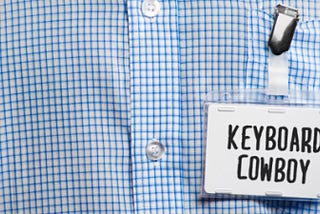 imagem de um crachá escrito Keyboard Cowboy, preso em uma blusa social xadrez azul