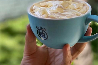 A blue coffee cup with ‘Bo Cafe’ written on it, held in someone’s hand.