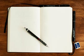 A blank journal laying open on a wood surface with a pen resting on top of the pages.