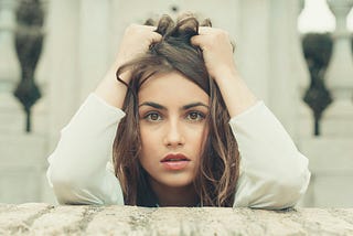 A woman, holding her hair, looks nervously into the camera.