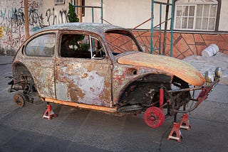 An old, rusty VW bug sits up on blocks. It’s in rough shape.