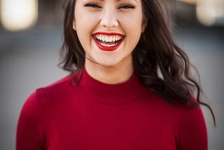 A young brunette lady wearing a red top and red lipstick smiling in ecstasy