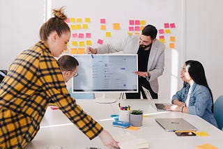 Four people working around a conference room table. One man pointing to a computer screen.