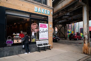 A Bakery Storefront by a bridge underpass, with a large poster display saying “CURBSIDE.”