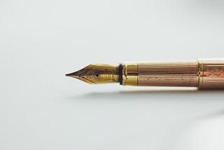 A classic fountain pen that shows signs of wear sits idle on a white surface. It has a gold tip and rose gold shaft.