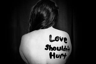 The naked upper back of a woman with the words “love shouldn’t hurt” painted on