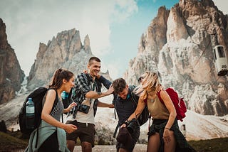 Four friends in hiking gear in front of a rocky cliff thing.