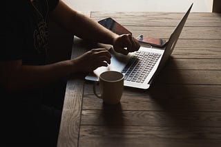 person doing content writing on laptop, coffee mug on the table