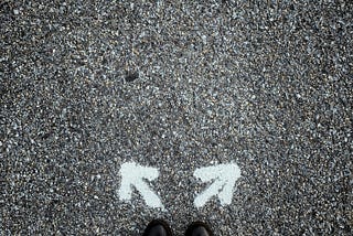 First person view of someone’s feet standing over two arrows pointing different directions.